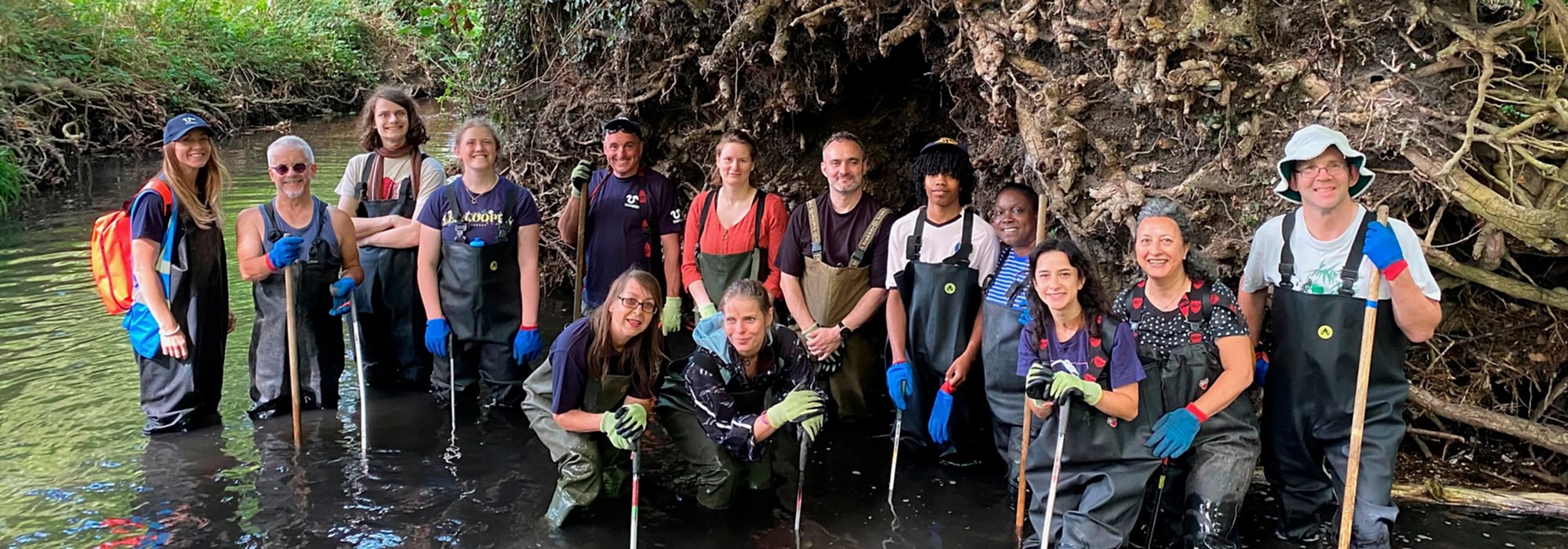 A group of adult volunteers in waders in a river looking to the camera