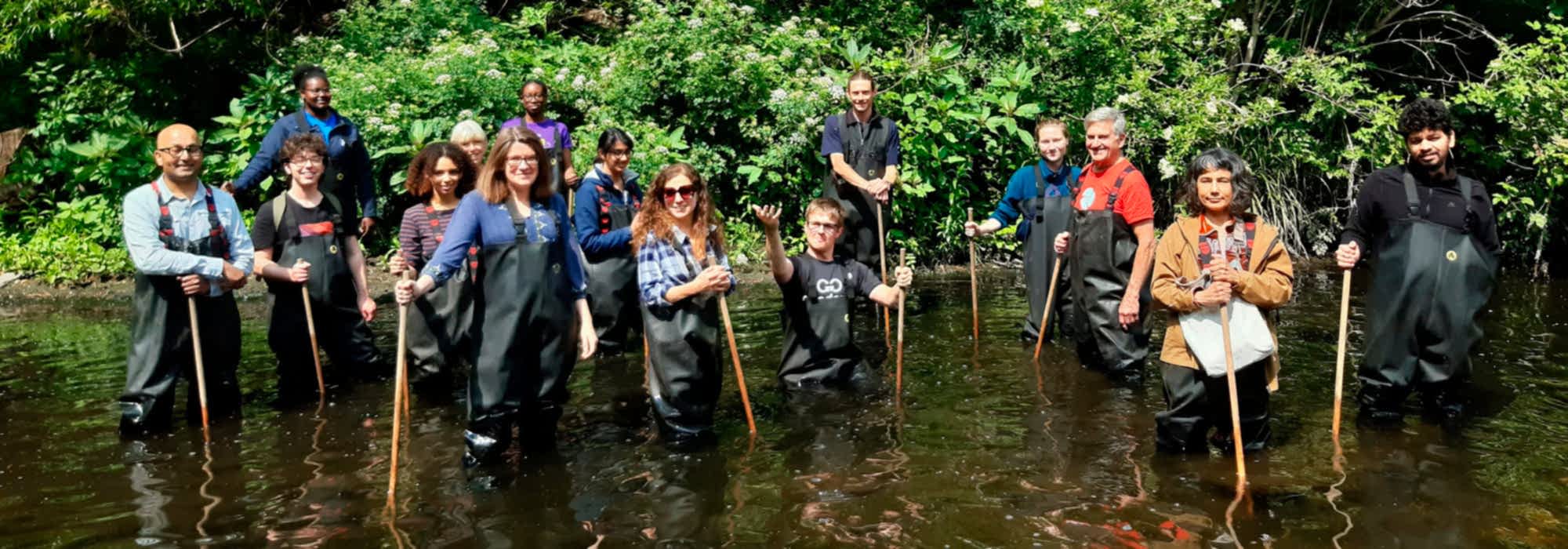 15 volunteers in waders standing knee deep in a river facing the camera and smiling